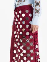 Pollera cruzada de largo midi, confeccionada en guipur negro con espejos circulares bordados. Presenta un lazo de ajuste en la cintura y forrería interna al tono.