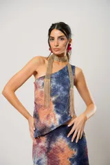 Conjunto de falda larga y top asimétrico con estampado tie-dye en tonos azul, naranja y marrón. El top es de un solo hombro y tiene un collarín con flecos dorados.