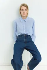 Camisa celeste y blanca a rayas verticales, confeccionada en mezcla de lino y viscosa. Tiene cuello clásico, botones frontales, bolsillo de parche en el pecho, mangas largas con puños abotonados y bajo redondeado.