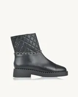 Bota corta negra de cuero con caña acolchada con diseño de rombos, detalle de cadena plateada y suela track con tachas.