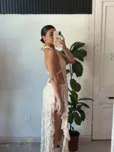 Vestido largo de encaje color nude, con escote halter y espalda descubierta. Incluye cinturón blanco con apliques metálicos.