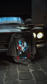 Remera negra con efecto nevado/acid wash, corte oversize, con estampado gráfico en la espalda inspirado en la película 'Bastardos sin gloria' de Tarantino, mostrando personajes con armas y dinamitas.
