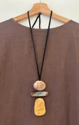 Collar largo con cordón de gamuza negro regulable y dije con tres piezas geométricas de acrílico con acabado marmoleado en tonos beige, marrón y dorado.