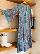 Kimono largo de seda con estampado floral en tonos verde, marrón y beige. Tiene mangas amplias y corte cruzado con lazo ajustable en la cintura.