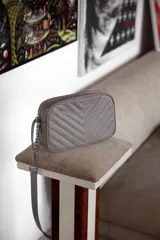 Cartera bandolera negra con diseño capitoneado en forma de V, correa de cuero y cadena plateada, cierre metálico y doble bolsillo interior.