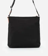 Bandolera negra de poliéster con detalles en cuero sintético color marrón. Tiene correa transversal ajustable, cierre de cremallera, bolsillos delanteros y placa metálica con el logo de la marca.