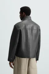 Cazadora cropped de piel negra, con cuello alto, cierre frontal con cremallera, bolsillos de parche en el pecho y puños con botón.