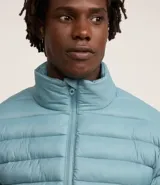 Campera puffer ultraligera color beige, con cuello alto, cierre por cremallera y bolsillos con cremallera. Incluye bolso de almacenamiento.