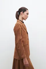 Blazer color tostado de similar gamuza, con diseño clásico de botones y corte entallado.