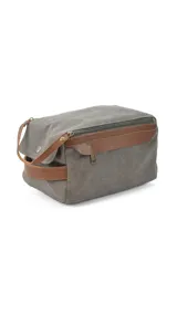 Neceser gris de tela canvas con detalles en cuero marrón. Tiene doble cierre, bolsillos internos con cierre y abiertos, bolsillo frontal con solapa y asa lateral.