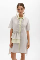 Vestido camisero a rayas verticales color gris y blanco, con cuello y cartera en lino color lima. Presenta volados frontales y laterales.