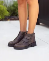 Botines de cuero marrón oscuro con efecto desgastado y suela track negra gruesa. El calzado se ajusta mediante dos tiras de velcro en el empeine.