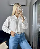 Camisa blanca de mangas largas con puños abullonados y detalles de encaje en cuello, mangas y ruedo.