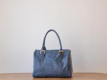 Bolso de mano azul con detalles de costuras verticales y herrajes dorados.