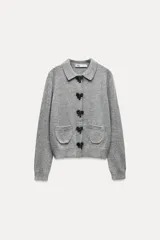 Chaqueta de punto gris con cuello solapa y manga larga. Tiene bolsillos delanteros de plastrón, rib en los acabados y cierre frontal con botones a presión en forma de lazo.