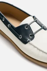 Zapato náutico de cuero blanco con detalles en negro y suela marrón.