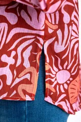 Blusa oversize de poliéster con estampado de animales y plantas en tonos rosa y marrón. Tiene cuello camisero, mangas largas y cierre frontal con lazos.