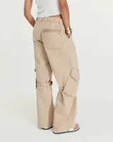 Pantalón cargo de gabardina gastada de lino y algodón color azul. Silueta de pierna recta ancha, con cartera con cierre metálico y broche níquel en el cruce de la cintura. Tiene bolsillos inclinados en los laterales y bolsillos cargo con tapa y broches metálicos a la altura de las rodillas, de los cuales salen unas tiras que se ajustan mediante hebillas metálicas para modificar la silueta del pantalón. En la espalda tiene pinzas y un bolsillo plaque con cierre metálico en boca. Es tiro medio.