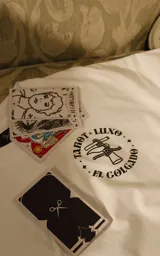Remera blanca de algodón con cuello redondo y calce oversize. Estampa en el frente con diseño de la carta del tarot 'El Colgado' y la leyenda 'Tarot x Luxo'.