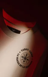 Remera blanca de manga corta con cuello redondo y calce oversize. Presenta una estampa en sublimación inspirada en el tarot, con la imagen de una figura femenina sosteniendo un salvavidas con la frase "Chill Bitch Trust Karma" y el texto "The Wheel of Fortune" en la parte inferior.