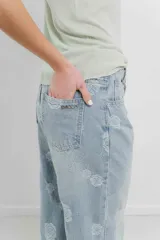 Pantalón de jean celeste de tiro alto y corte ancho, con bordado de flores grandes en hilo blanco hueso.