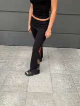 Pantalón negro de tejido de punto con aberturas en la parte inferior de la pierna con apliques de cuero marrón.