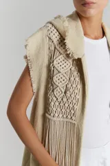 Chaleco largo color beige de tejido rústico de algodón con macramé aplicado y capucha. Terminaciones al corte, desflecadas.