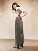 Falda larga de jean color gris oscuro, con corte en A y costuras verticales decorativas en el frente. Tiene bolsillos laterales y cierre con botón y cremallera.