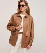 Campera estilo safari o sobrecamisa de mujer, color marrón camel, confeccionada en tejido que simula gamuza o cuero sintético. Presenta cuello camisa, cierre frontal de botones a presión, y cuatro bolsillos frontales con tapa (dos en el pecho y dos a la altura de la cadera). Tiene costuras visibles que definen el diseño.