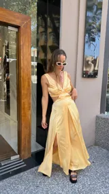 Vestido largo color durazno con escote pronunciado en V y aberturas laterales en la cintura. Presenta un drapeado frontal y falda con tajo lateral.