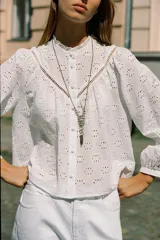 Camisa blanca de manga larga con cuello con volantes y bordados perforados. Cierre frontal con botones a tono.