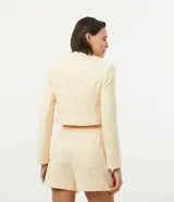 Blazer cropped color amarillo pastel, de crepé con forro de poliéster, cuello solapa, manga larga y cierre frontal con botón en forma de corazón.