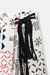 Falda midi de tiro alto confeccionada en hilatura con lino, color blanco con estampado geométrico en tonos marrones y rojizos. Cierre frontal cruzado con lazada a contraste en color negro.