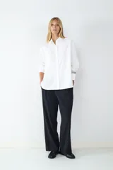 Camisa blanca de popelina de algodón, de corte amplio, manga larga, cuello clásico, cierre frontal con botones y puños abotonados.