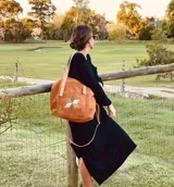 Bolso tipo tote de gamuza color camel, con aplique de estrella geométrica en tonos blanco, verde y marrón. Tiene doble asa de cuero al hombro y correa bandolera extraíble y ajustable. El interior está forrado en gamuza y cuenta con bolsillo con cierre y llavero.