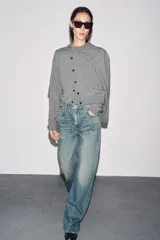 Chaqueta de punto color rosa pálido, con cuello redondo y cierre frontal de botones oscuros. Presenta mangas largas y un corte a la cintura.