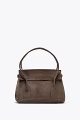 Bolso marrón de gamuza sintética, tipo city bag, con doble asa de hombro y cierre con solapa e imán. Tiene correa ajustable con hebillas metálicas en los laterales y bolsillo interior con cremallera.