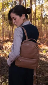 Mochila marrón claro de símil cuero con bolsillo ojal al frente con cierre y broche, apertura superior con cierres metálicos, bolsillos laterales y bolsillos internos. Incluye correas regulables para colgar en la espalda, asa de mano y correa adicional para llevar colgada al frente.