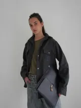 Camisa gris de lana con corte clásico, cuello camisero, cierre frontal con botones de cuerno y dos bolsillos de parche en el pecho.