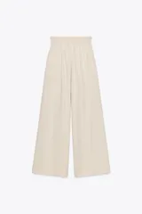 Pantalón palazzo color crudo, confeccionado en tejido fluido con mezcla de lyocell. Presenta tiro medio, cintura elástica ajustable con cordones, bolsillos laterales ocultos en costura y pierna ancha.
