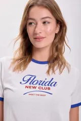 Remera blanca de algodón con cuello y mangas con ribete azul. Estampa frontal con la palabra "Florida" en azul y "New Club" en rojo.