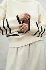 Sweater color crema con rayas horizontales negras en el pecho y los puños, de corte holgado y cuello redondo.