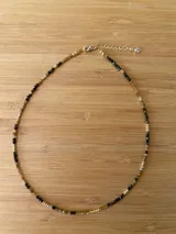 Gargantilla corta con cuentas facetadas de color marrón, negro y dorado, con cierre de mosquetón y cadena de extensión dorada.