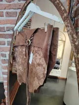 Top de cuero marrón con diseño artesanal, ajuste regulable con cordones en la espalda y detalle de argolla metálica.
