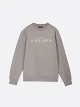 Buzo gris de Tommy Hilfiger con cuello redondo, corte regular y hombros ligeramente caídos. Presenta el logo de la marca estampado en el pecho y un logo bordado en el puño.