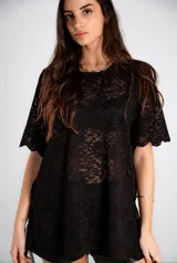 Remerón o vestido corto de encaje negro, con mangas cortas y terminaciones festoneadas. El tejido es transparente.