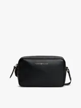 Cartera tipo cámara cruzada (crossbody) color negro, con acabado liso y logo metalizado de Tommy Hilfiger en el frente. Posee un compartimento principal con cierre de cremallera y un asa tejida ajustable.