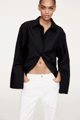 Camisa negra oversized de algodón con cuello clásico, abotonadura frontal, mangas largas con hombros caídos, puños con abertura y bajo recto.