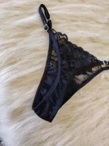 Conjunto de lencería negro de encaje, compuesto por un bralette con breteles regulables y una tanga regulable con corte cola less y entrepierna de algodón.