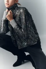 Camisa de cuero ovino con estampado de piel de serpiente multicolor y detalles metalizados. Presenta un cuello alto, botones a presión con logo de alas y puños de tejido de punto gris.